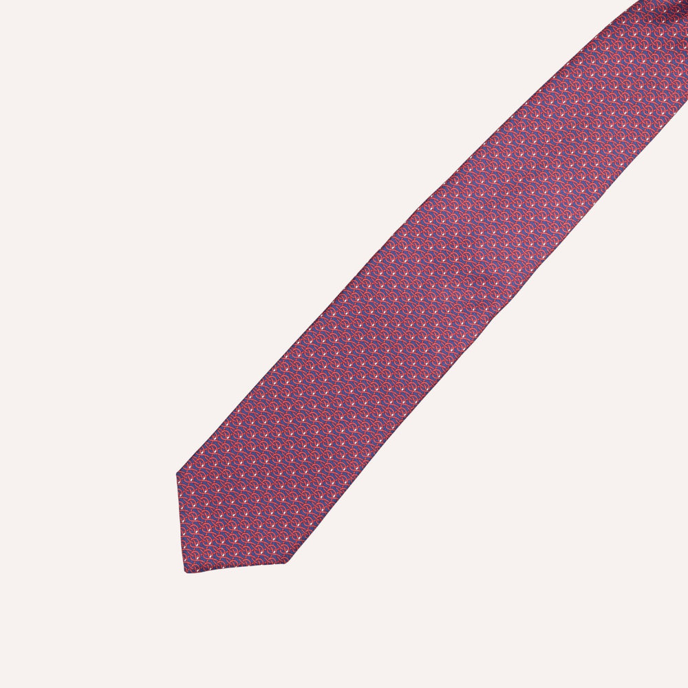 A classic necktie with a repeating micro-pattern of small blue and red geometric shapes on a deep purple base, laid diagonally on a light cream background.