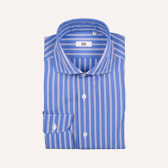 A folded blue dress shirt with white vertical pinstripes, featuring a pointed collar, button-down front, and a single cuff, displayed on a light cream background.