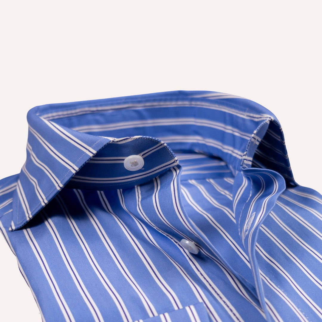 A close-up of a blue button-down shirt with thin white vertical pinstripes, showing the collar, button, and fabric texture against a light off-white background.