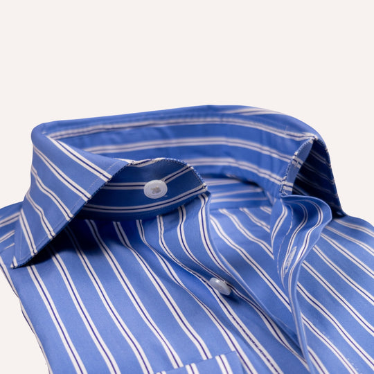 A close-up of a blue button-down shirt with thin white vertical pinstripes, showing the collar, button, and fabric texture against a light off-white background.