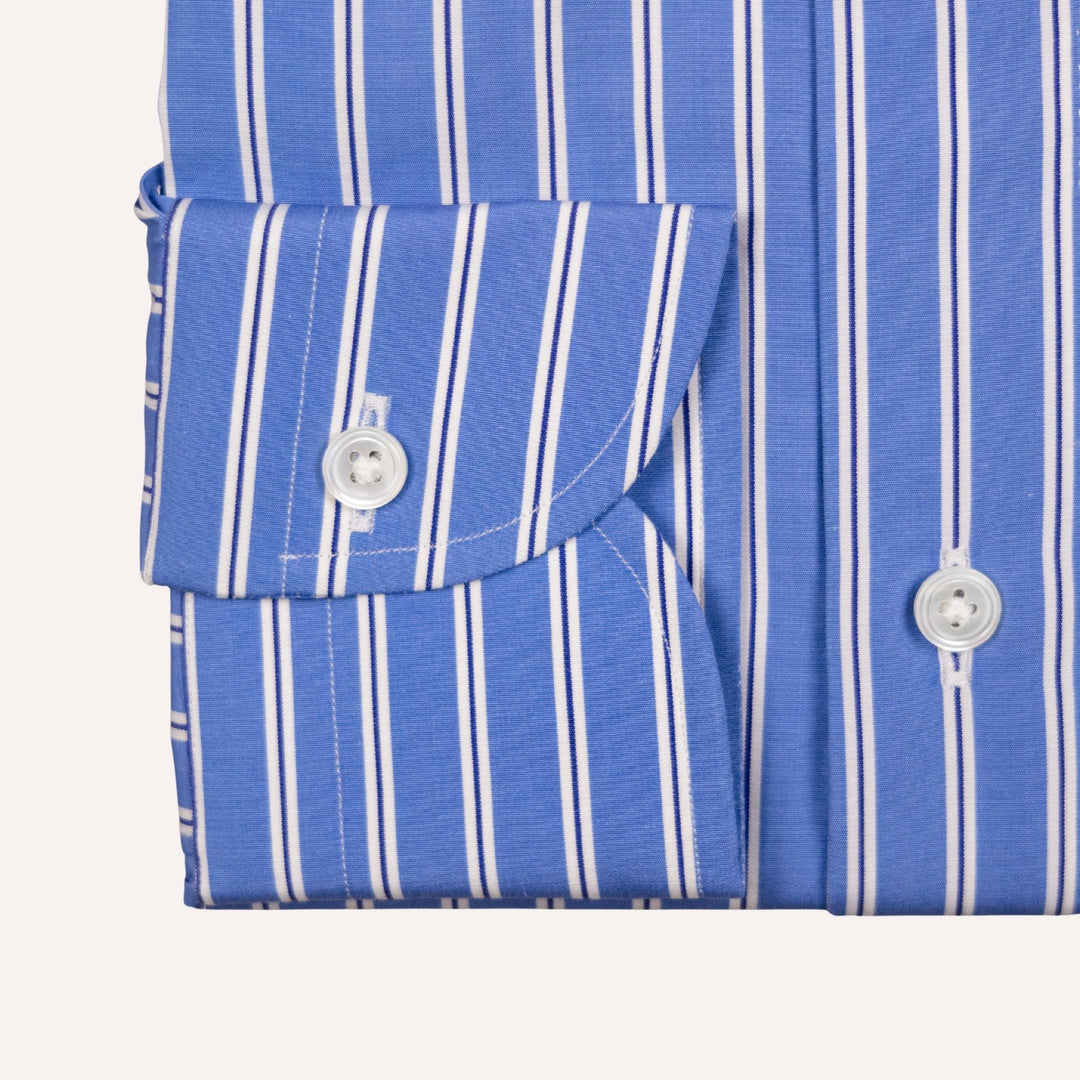 Close-up of a blue and white vertically striped shirt cuff with a buttoned pocket flap and white buttons on a light beige background.
