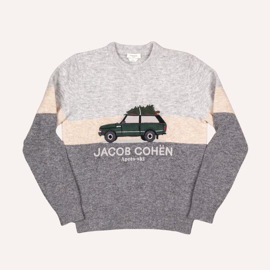 A colorblock crewneck sweater by Jacob Cohén, featuring a heather gray upper chest and shoulders, beige horizontal bands, and a dark gray lower body and sleeves. The center of the chest displays a graphic of a green station wagon carrying a Christmas tree, with 'JACOB COHÉN Après-ski' printed in white below it.