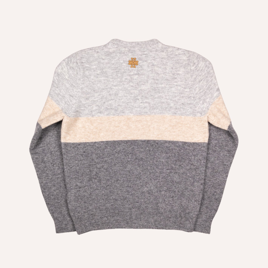 A color-blocked knit sweater shown from the back, featuring a light heather gray upper section, a wide cream horizontal stripe across the middle, and a darker heather gray lower section and sleeves. A small gold cross logo is centered below the neckline.
