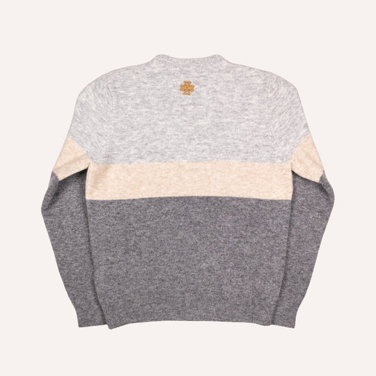 A color-blocked knit sweater shown from the back, featuring a light heather gray upper section, a wide cream horizontal stripe across the middle, and a darker heather gray lower section and sleeves. A small gold cross logo is centered below the neckline.