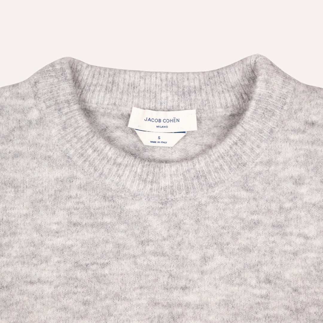 Close-up of a light gray heather knit crewneck sweater with a visible white neck label reading JACOB COHËN.