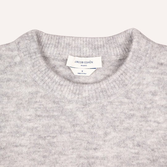 Close-up of a light gray heather knit crewneck sweater with a visible white neck label reading JACOB COHËN.