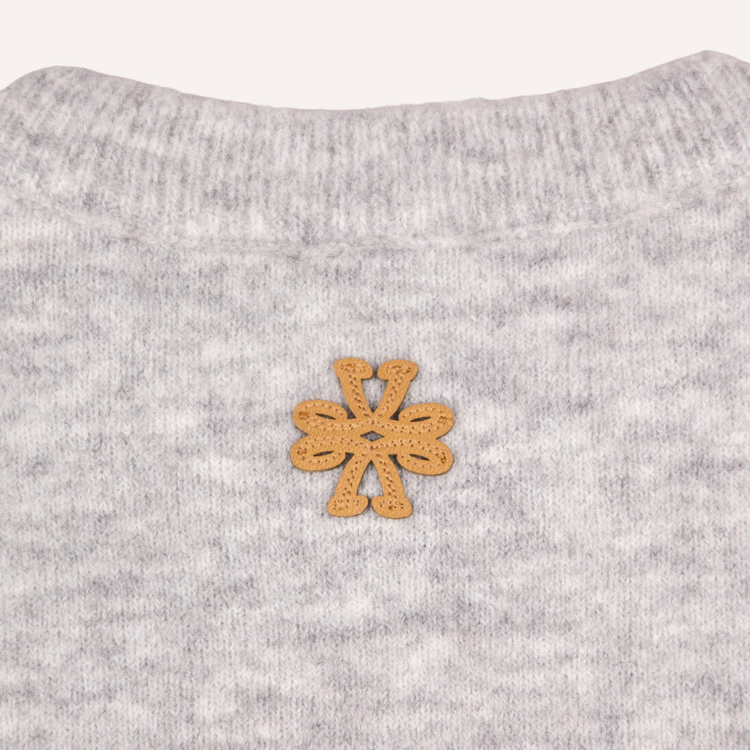 Close-up of a light gray heather knit garment with a small tan suede flower-shaped patch centered on the chest.