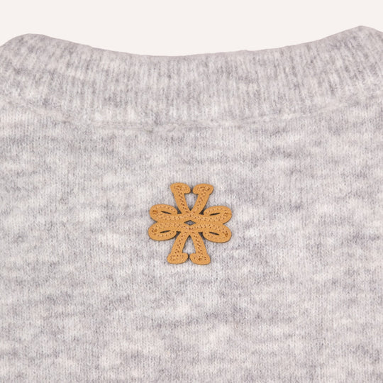 Close-up of a light gray heather knit garment with a small tan suede flower-shaped patch centered on the chest.