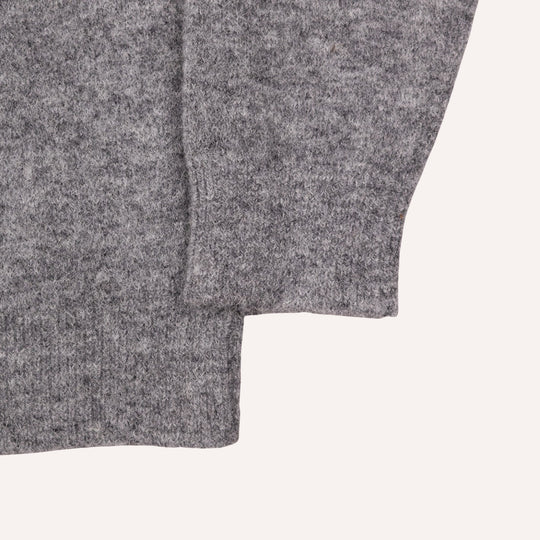 Close-up of a heather gray knit fabric, showing the texture and folded cuff of a sweater or garment on a light off-white background.