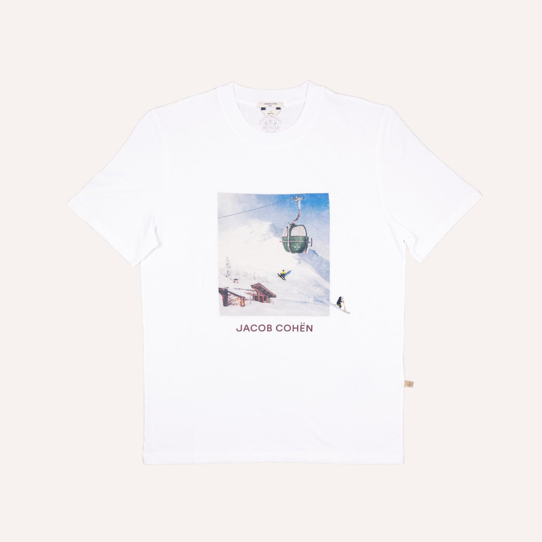 A white short-sleeve crewneck t-shirt featuring a square graphic print of a ski resort scene with a gondola and the text 'JACOB COHÉN' printed below it, displayed flat against a light beige background.