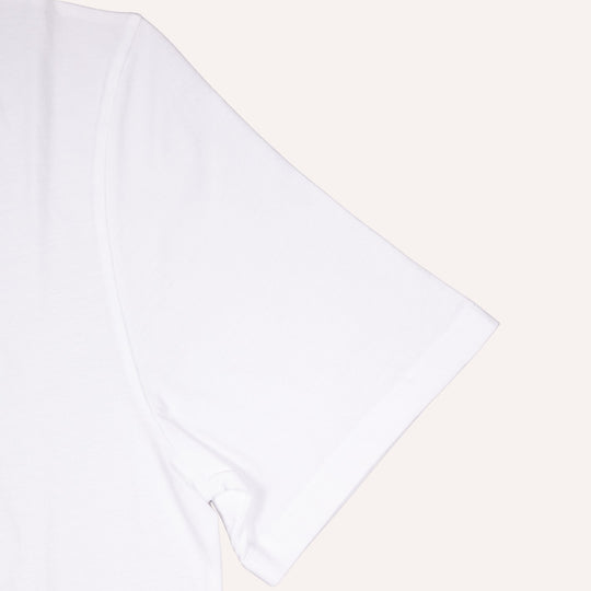 A close-up of a plain white short-sleeve t-shirt showing the sleeve and shoulder seam, set against a solid off-white background.