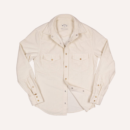 An off-white long-sleeve corduroy western shirt with two chest flap pockets and brass buttons, laid flat against a light cream background.