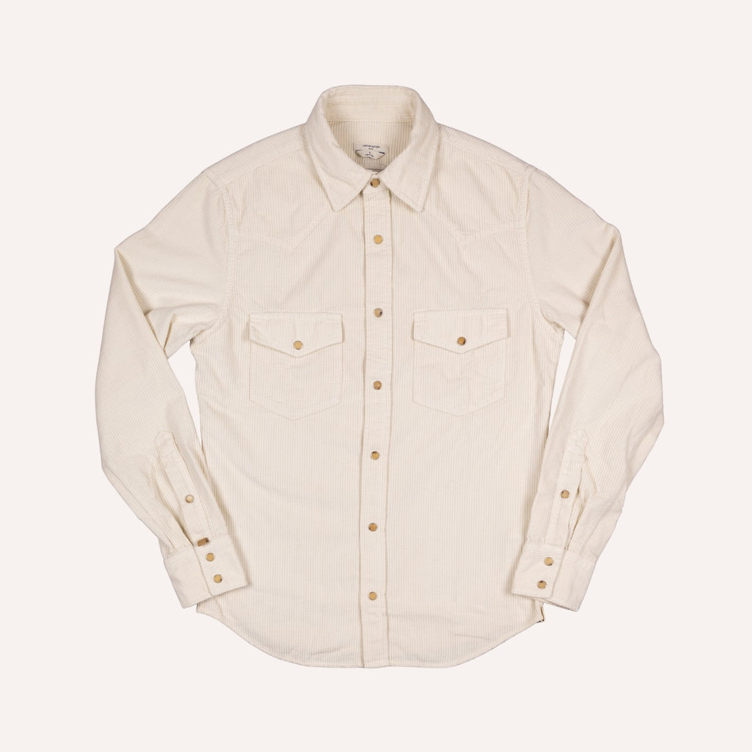 An off-white long-sleeve corduroy western shirt with two chest flap pockets and brass buttons, laid flat against a light cream background.