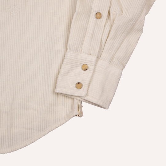 Close-up of a cream-colored corduroy shirt sleeve with three snap buttons on the cuff, set against a solid off-white background.