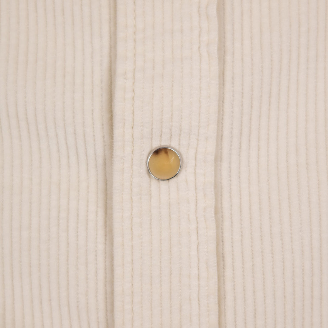 Close-up of a cream-colored ribbed fabric garment with a single round amber-yellow button with a silver metal rim.