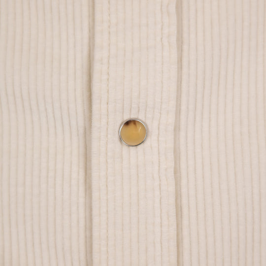 Close-up of a cream-colored ribbed fabric garment with a single round amber-yellow button with a silver metal rim.