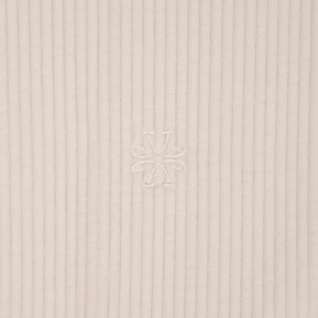 Close-up of a ribbed knit fabric in a light warm beige or cream tone, with a subtle tonal embroidered logo at the center.