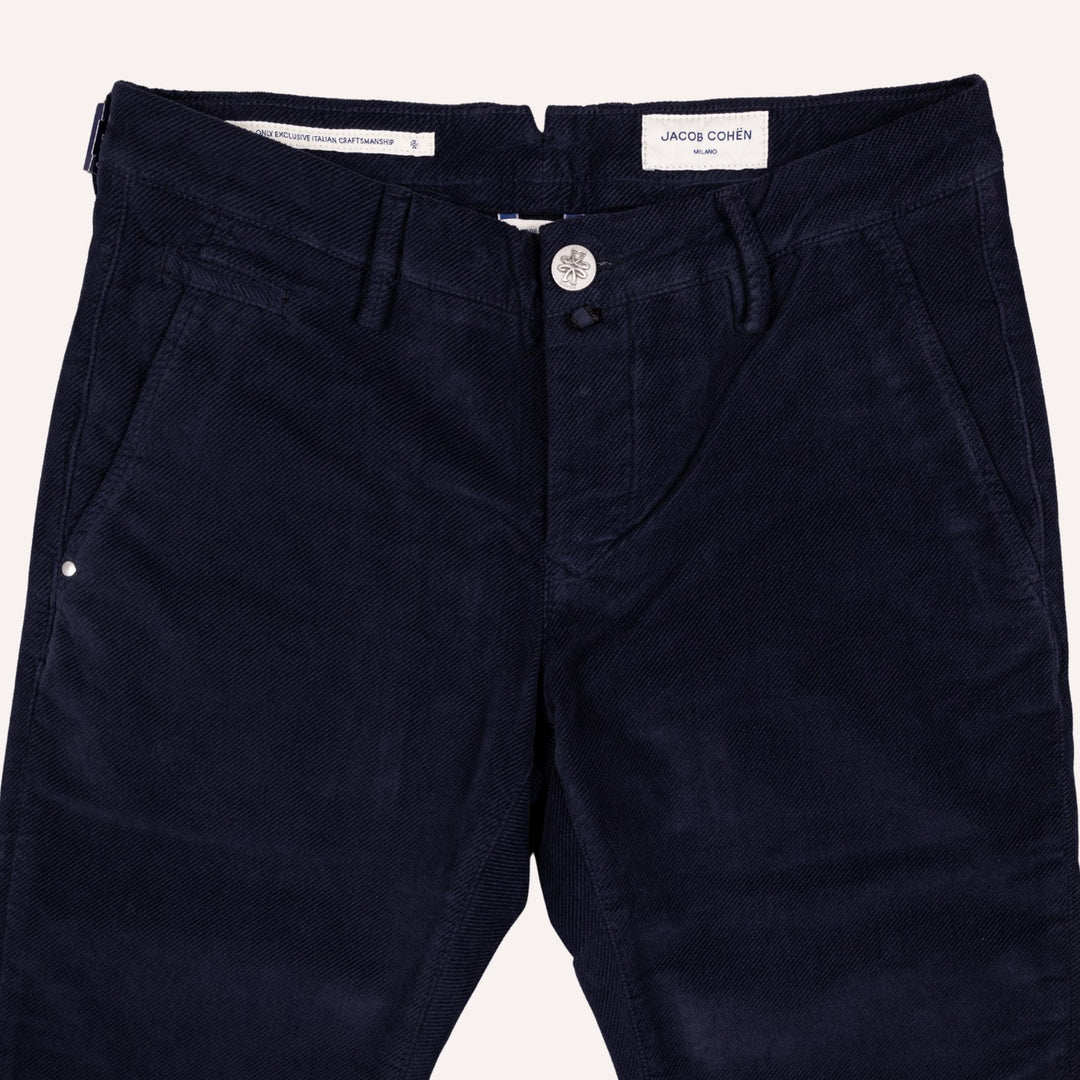 A close-up of dark navy blue twill trousers by Jacob Cohen, showing the front waistband, button closure, belt loops, and side pockets against a light off-white background.