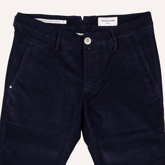 A close-up of dark navy blue twill trousers by Jacob Cohen, showing the front waistband, button closure, belt loops, and side pockets against a light off-white background.