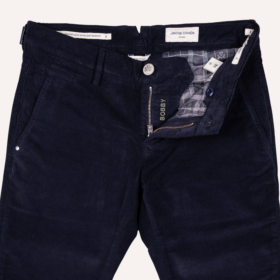 Close-up of dark navy twill trousers by Jacob Cohen, showing the front waistband, button closure, zippered fly, and interior plaid lining.