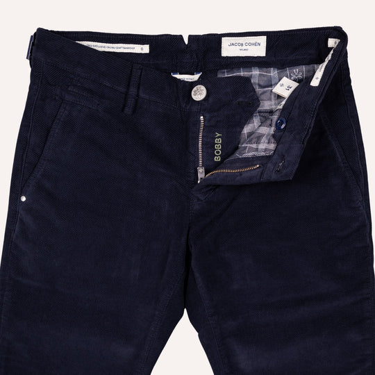 Close-up of dark navy twill trousers by Jacob Cohen, showing the front waistband, button closure, zippered fly, and interior plaid lining.