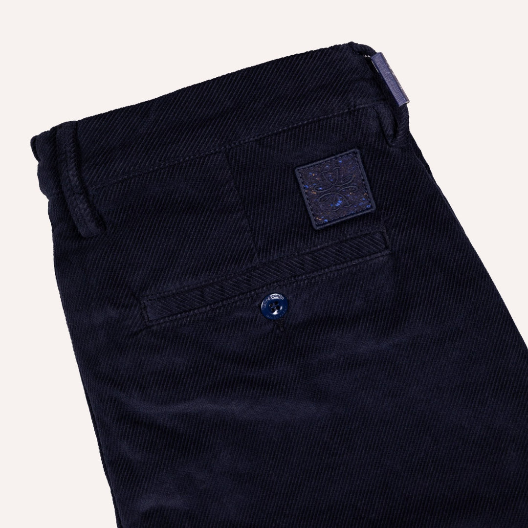 Close-up of dark navy twill trousers showing the back waistband, belt loops, a back pocket with a decorative button, and a textured brand patch.