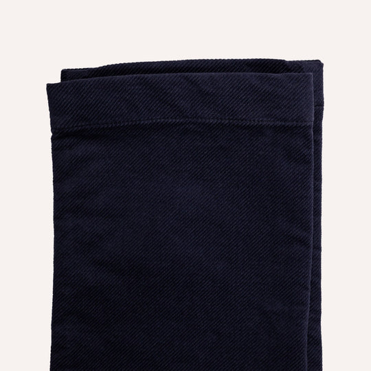 A close-up of folded dark navy blue fabric, showing a textured twill weave and neat hem stitching, set against a solid off-white background.