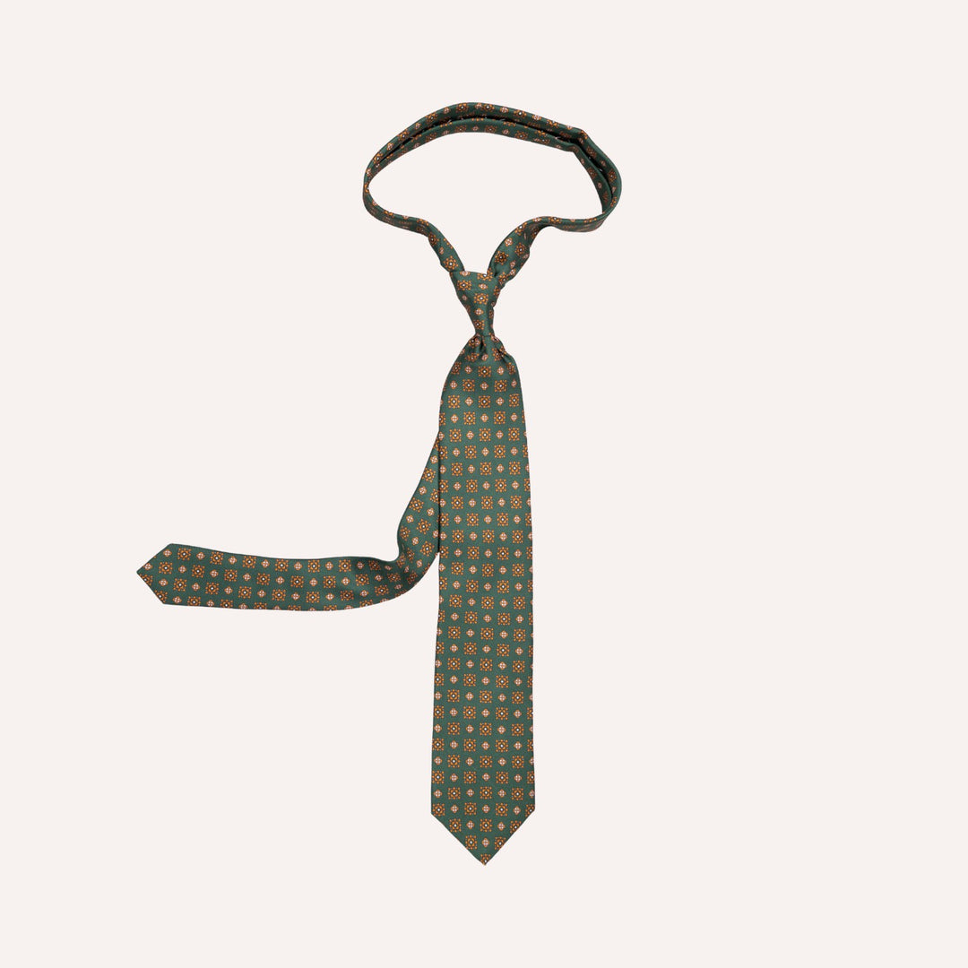 A dark green necktie with a repeating pattern of small orange and yellow flowers, laid flat on a light cream background.