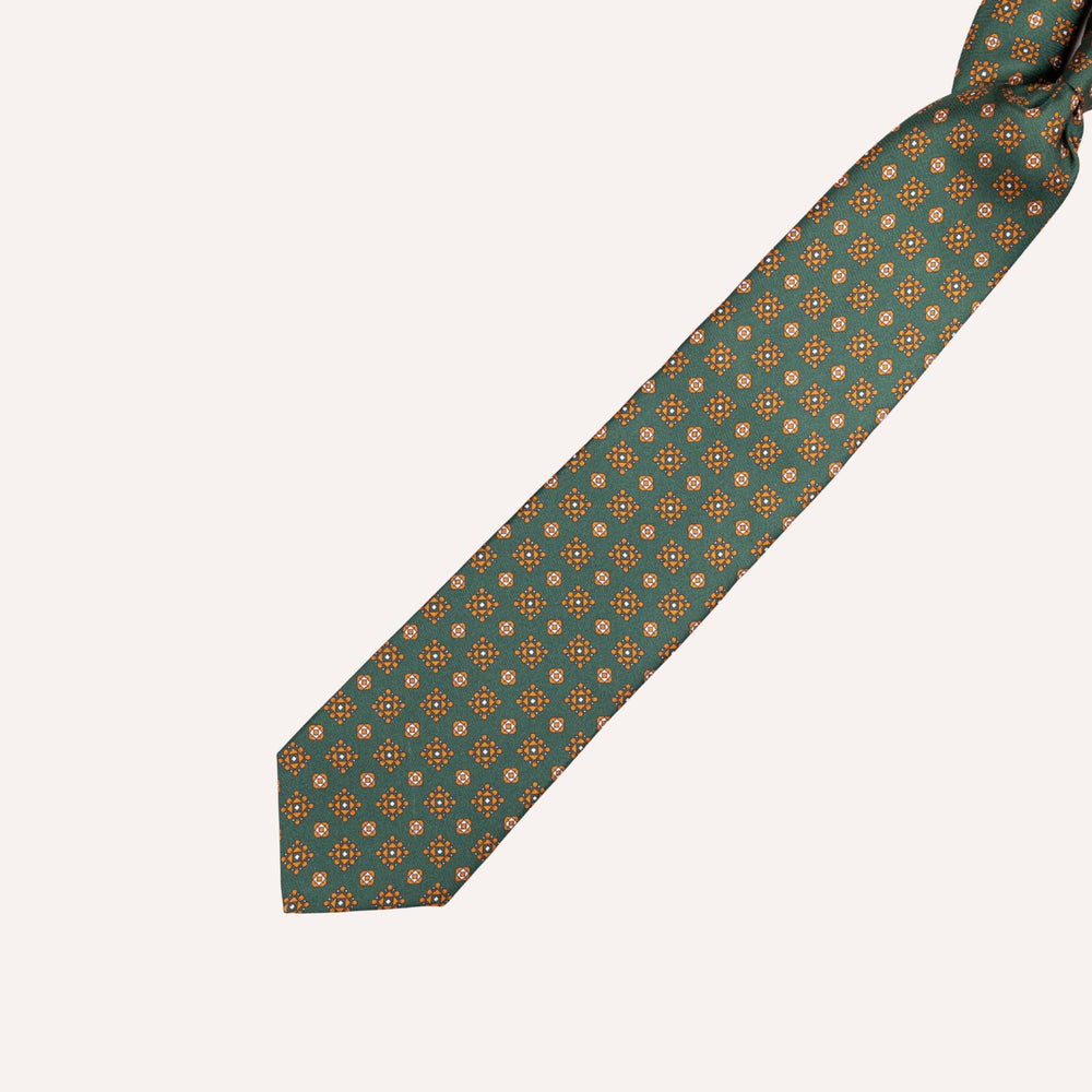 A dark teal necktie with a repeating geometric pattern of small orange and white circles, laid diagonally on a light cream background.