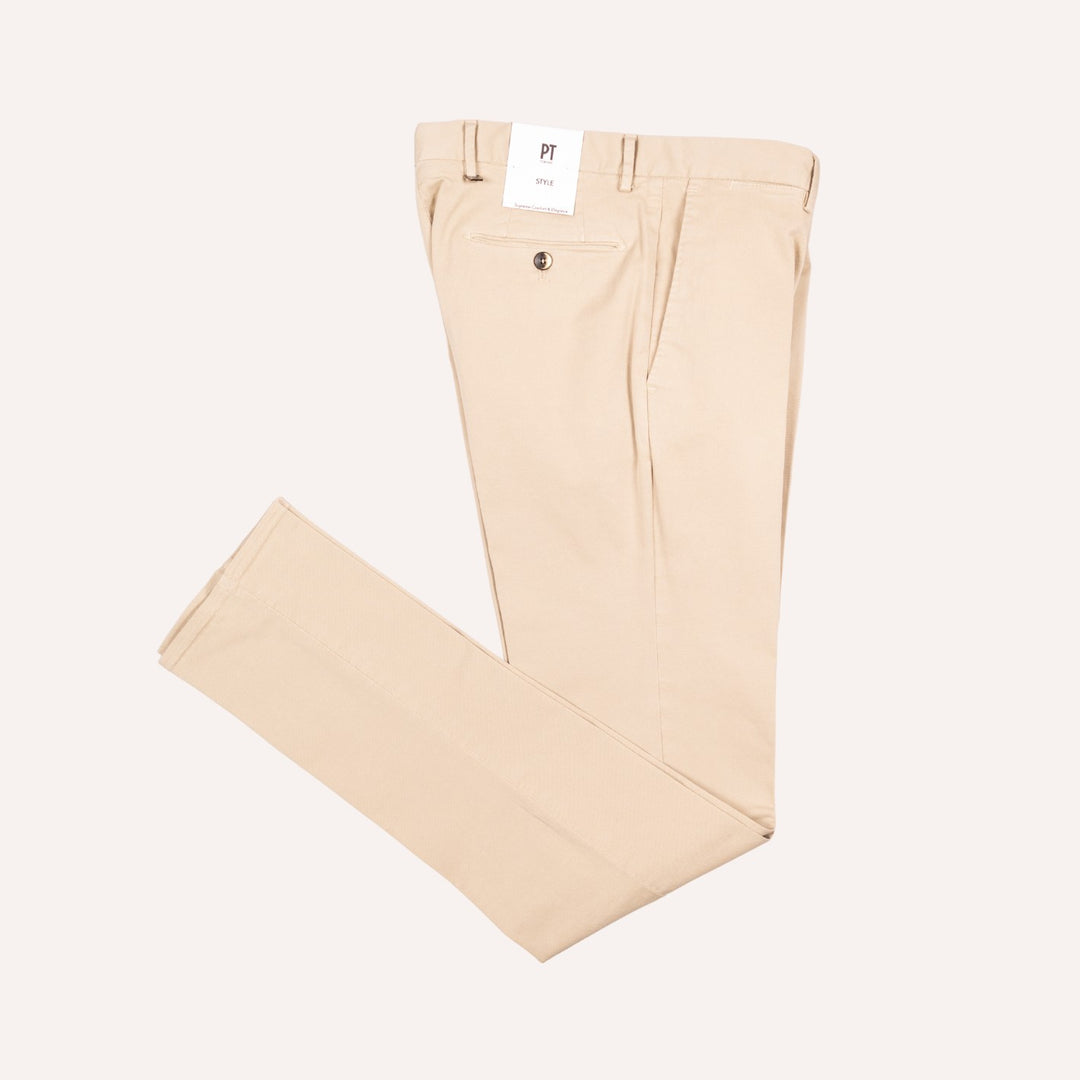 A pair of light beige chino pants laid flat on a light cream background, with a white brand tag visible at the waistband.