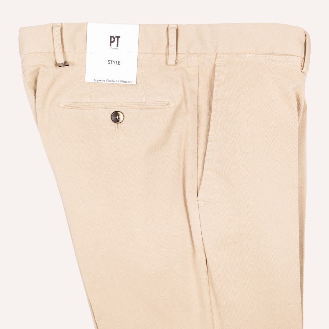 Close-up of the back waistband and rear pocket area of beige chino pants, showing belt loops, a white PT Style paper tag, and a single button closure.