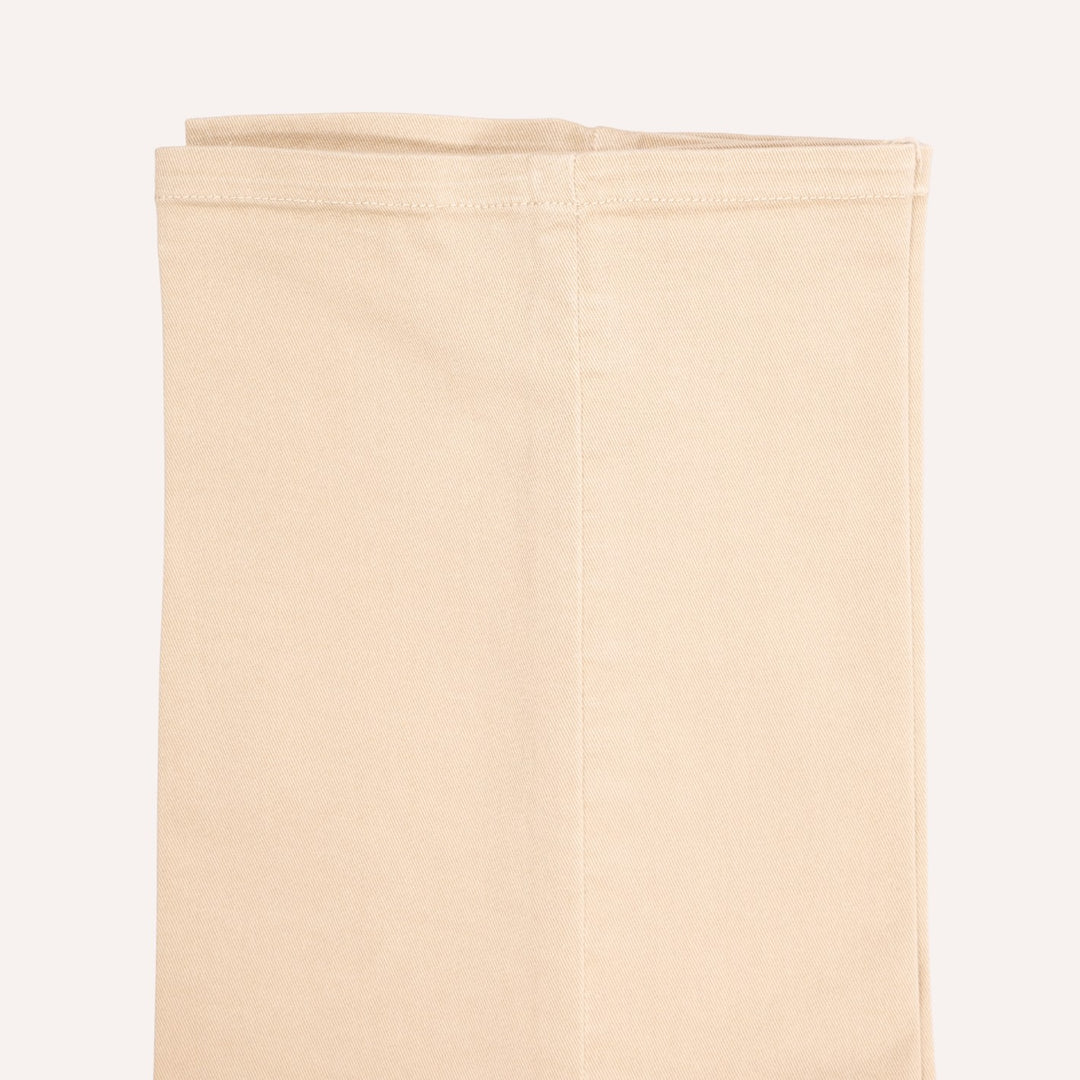 A folded beige trouser, shown against a solid off-white background.