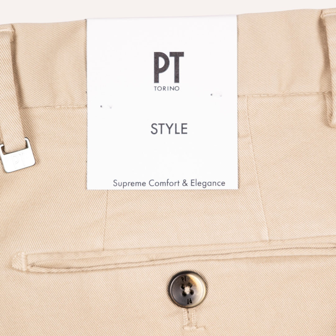 Close-up of beige trousers showing the waistband, a white PT Torino Style paper tag, and a horn button.
