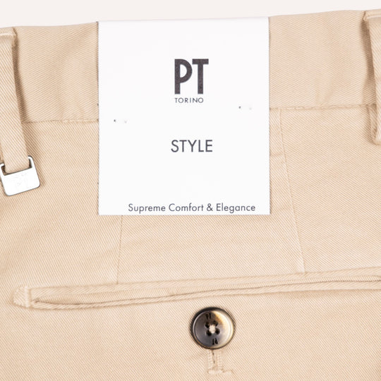 Close-up of beige trousers showing the waistband, a white PT Torino Style paper tag, and a horn button.