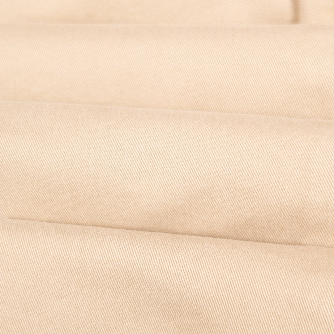 A close-up of folded beige fabric with a fine diagonal twill texture.