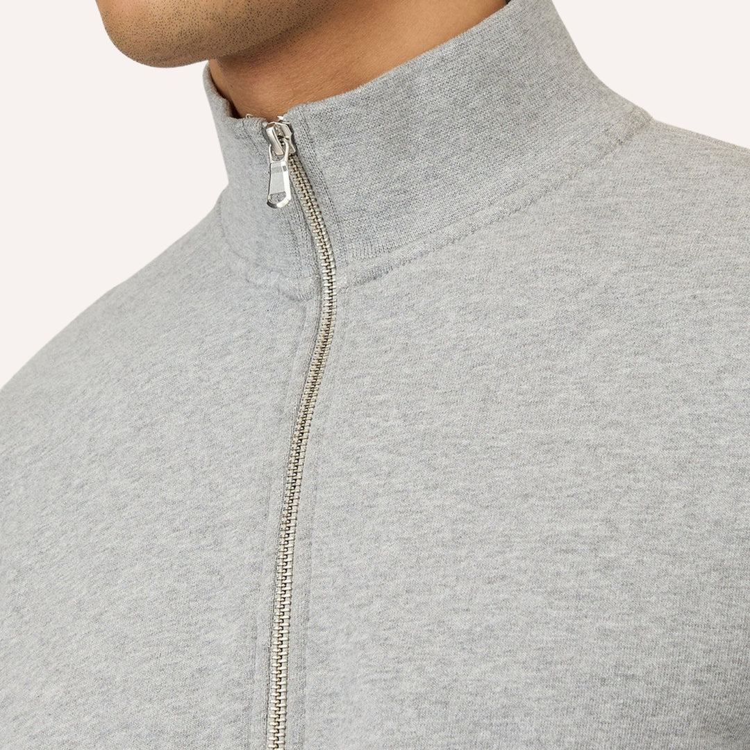 Close-up of a light gray heathered zip-up sweatshirt worn by a model, showing the collar, zipper, and fabric texture against a plain light background.