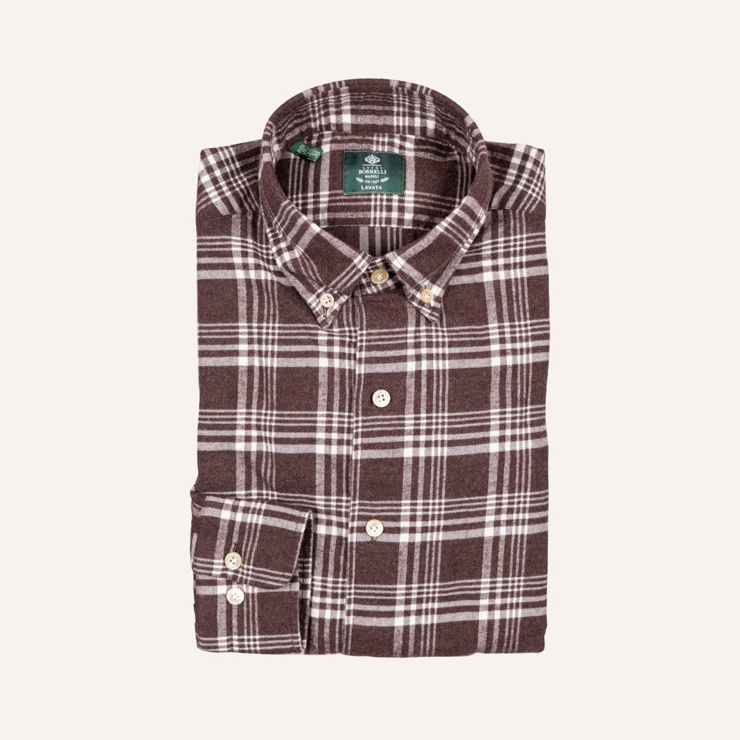 A folded brown and white plaid button-down shirt with a green neck label, displayed on a light cream background.