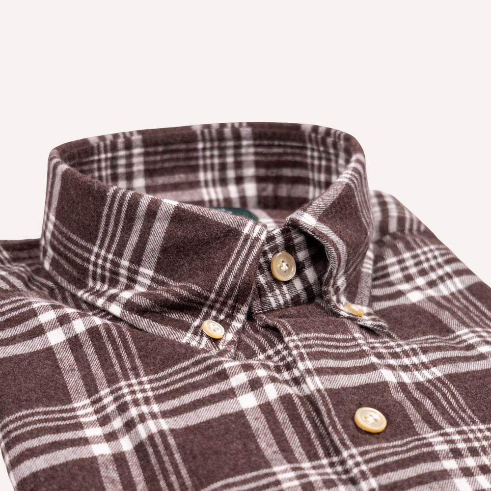 Close-up of a brown and white plaid button-down shirt collar with gold buttons on a light beige background.