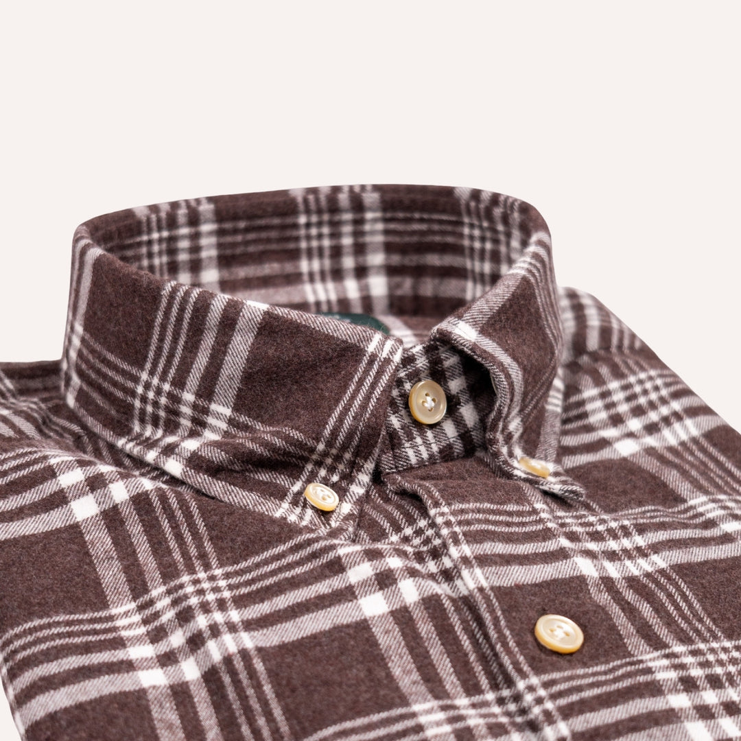 Close-up of a brown and white plaid button-down shirt collar with gold buttons on a light beige background.