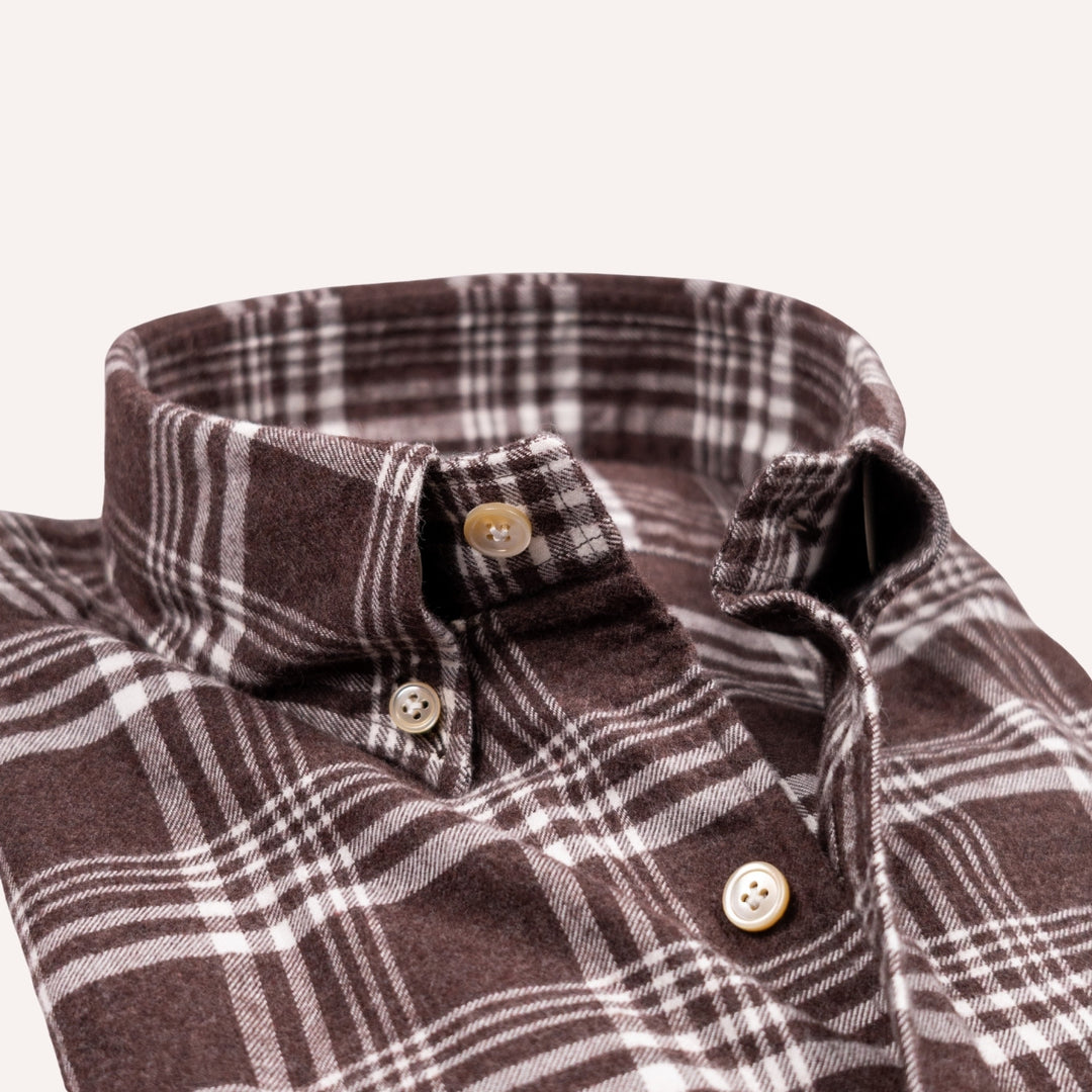 Close-up of a brown and white plaid button-down shirt collar with matching buttons, shown on a light cream background.