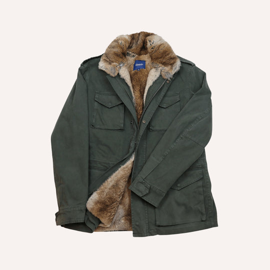 An olive green military-style parka jacket with a thick brown and beige rabbit fur collar lining, displayed flat against a light cream background.
